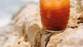 A glass of iced tea with an orange slice on a rock by the ocean.