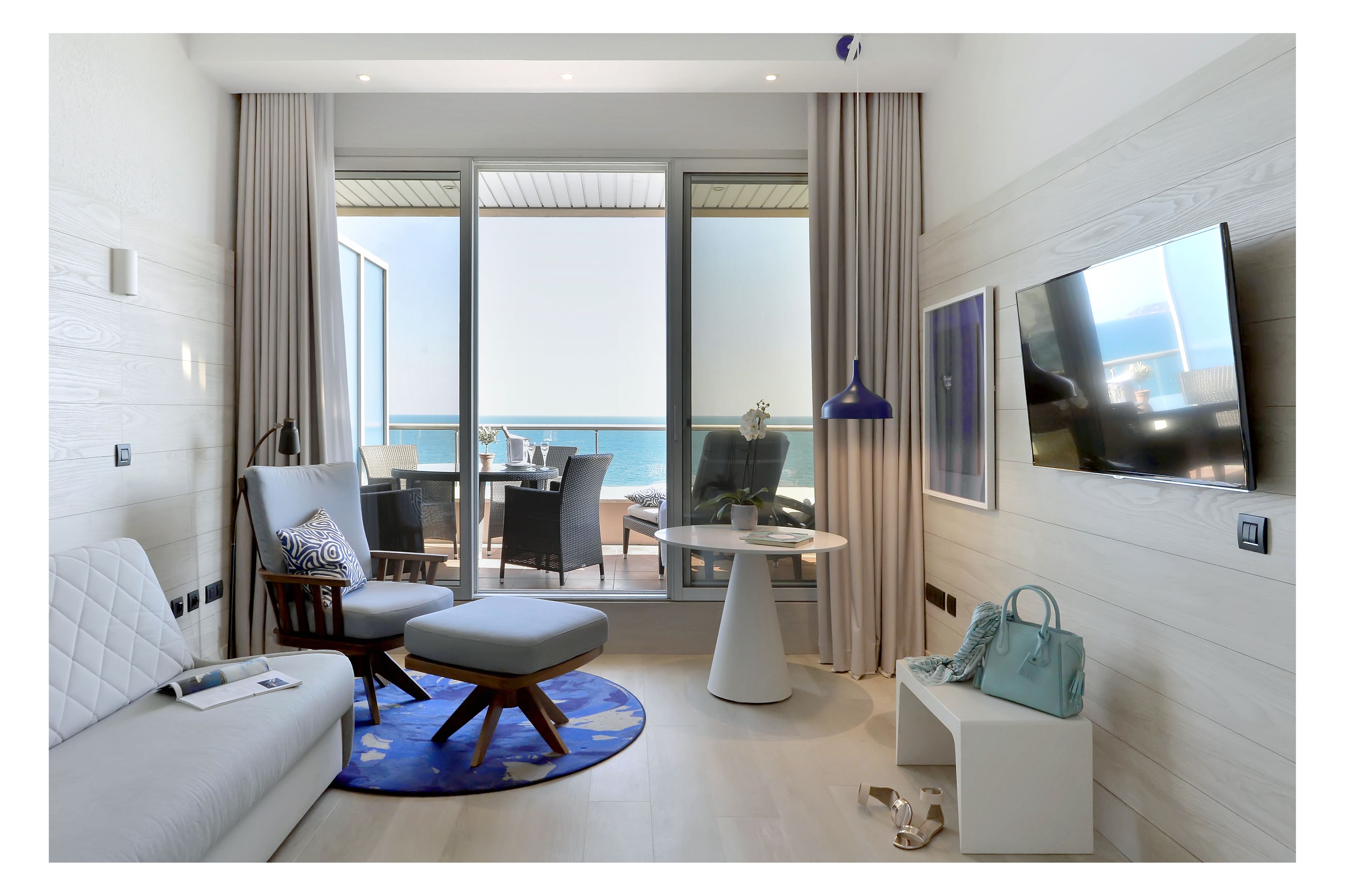Een moderne hotelkamer met balkon, een bank, een stoel, een ronde tafel en een televisie.