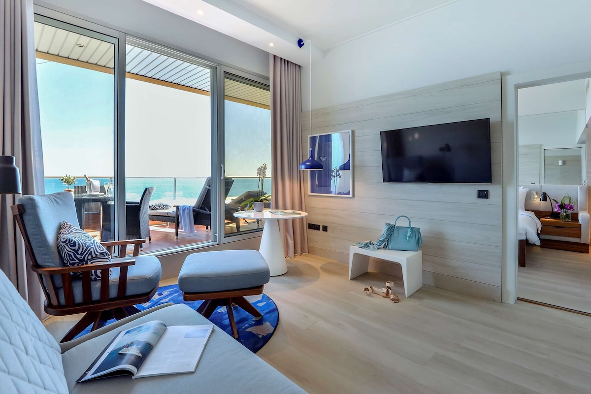 A modern living room with a large TV, comfortable seating, a balcony with a view, and a small table with a plant.