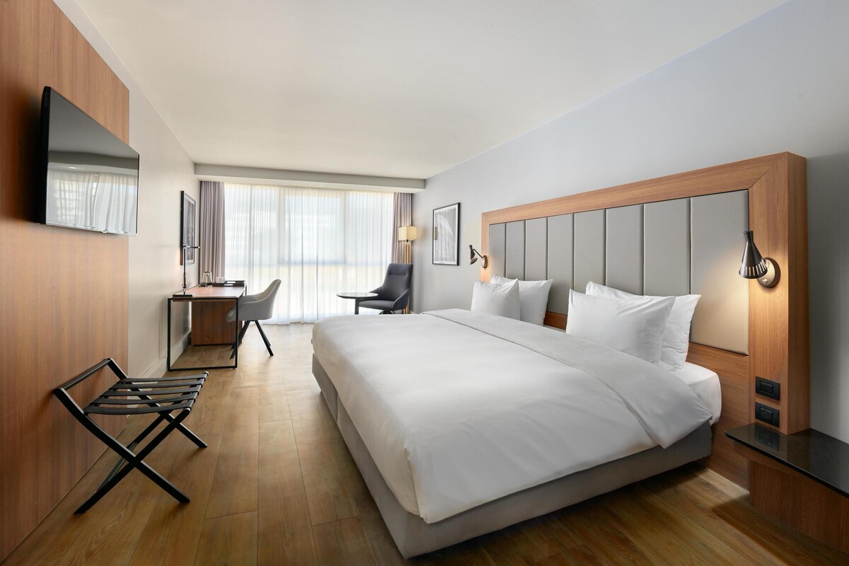 Ein modernes Hotelzimmer mit einem großen Bett, einem Schreibtisch, einem Sessel und einem an der Wand befestigten Fernseher.