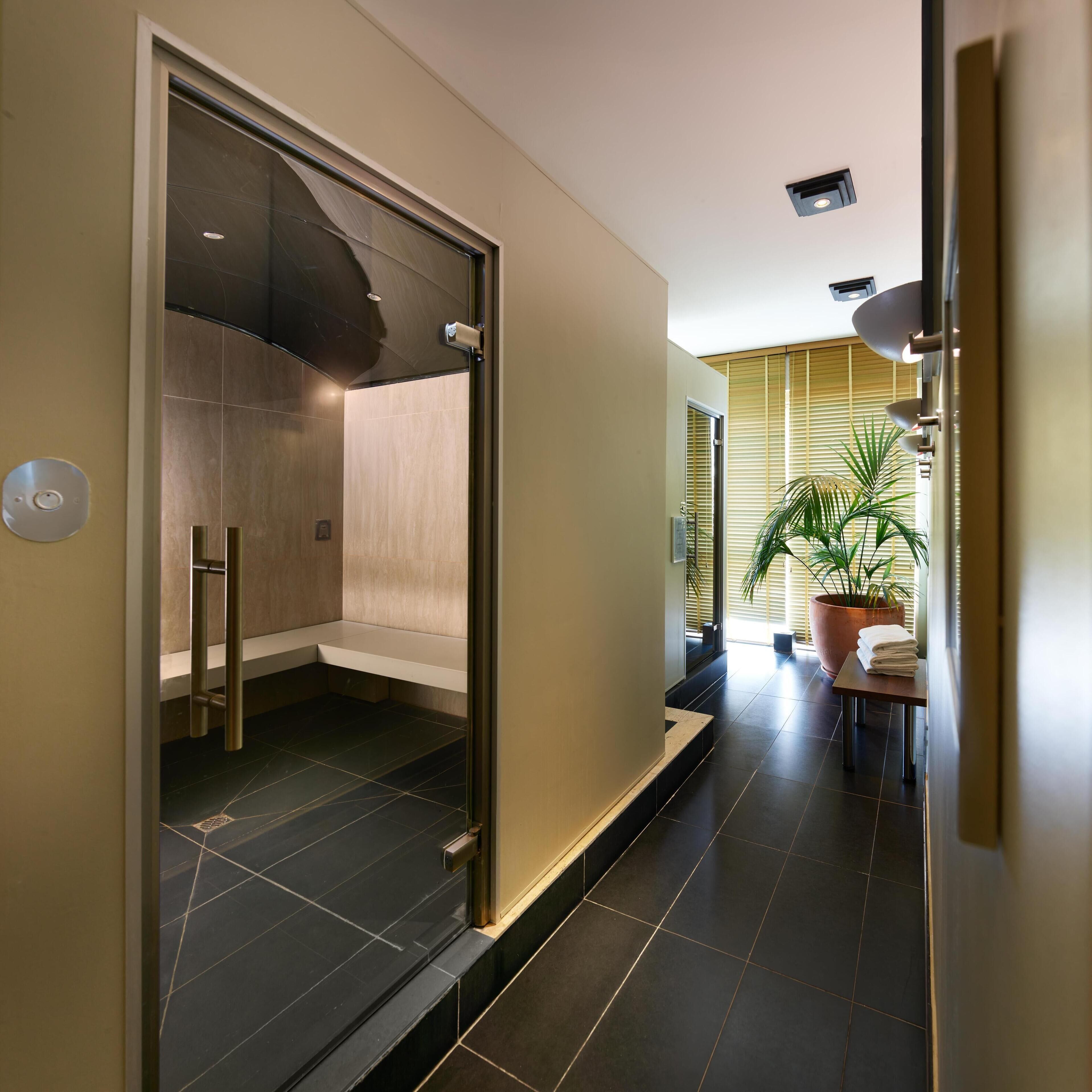 Een moderne badkamer met een glazen douchecabine, een bankje en een handdoekhouder.