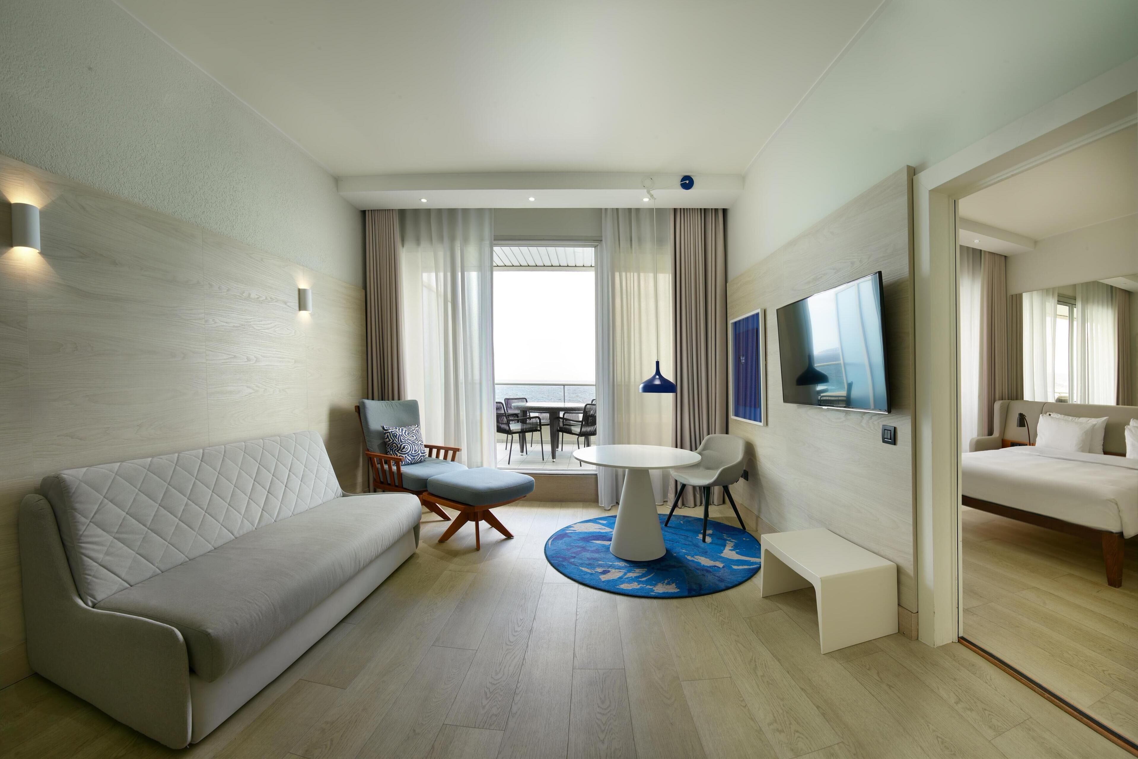 Una habitación de hotel moderna con sofá, una pequeña mesa de comedor, televisor y cama.