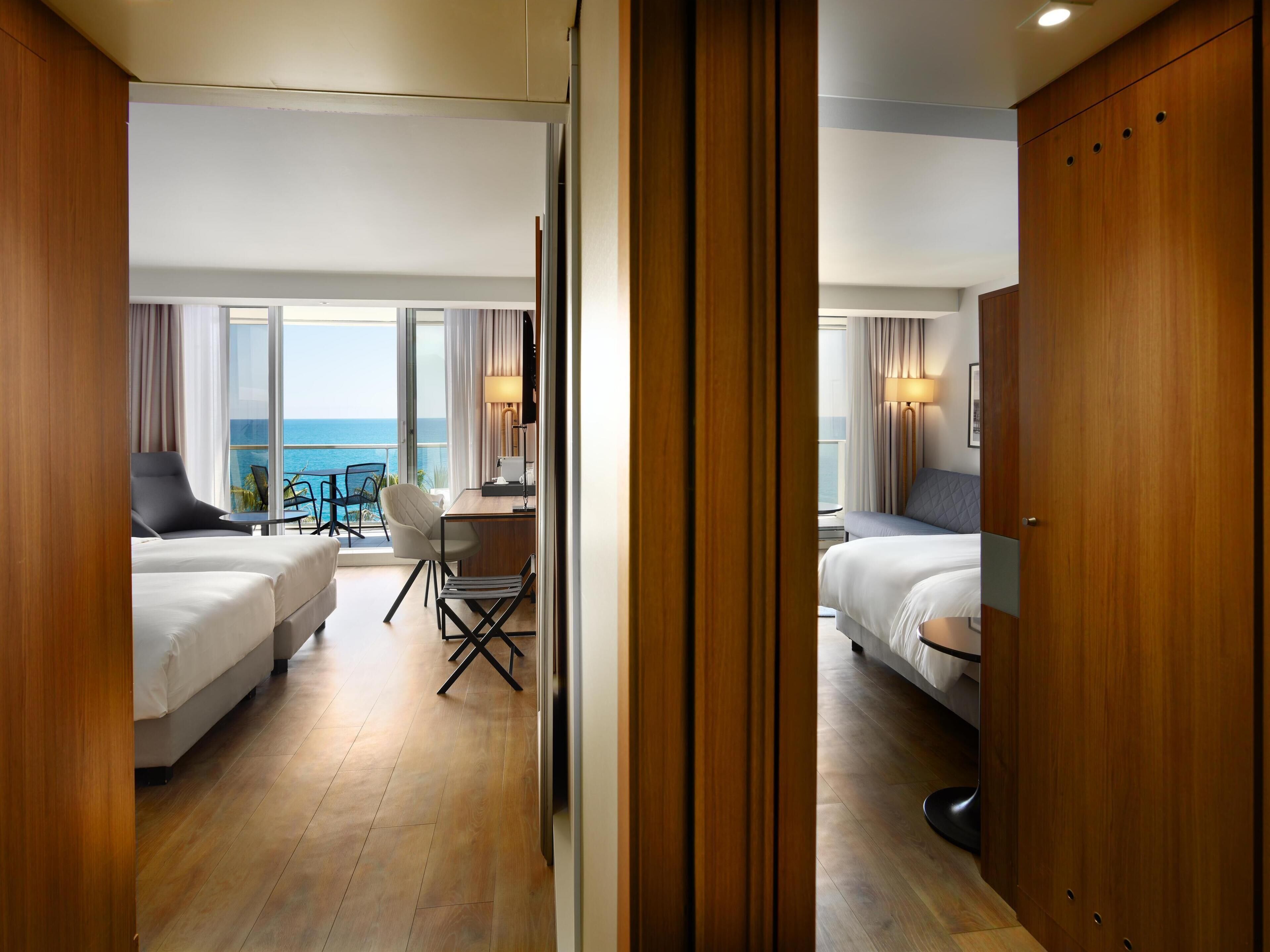 Habitación de hotel con dos camas, un escritorio, una silla y vista al océano.