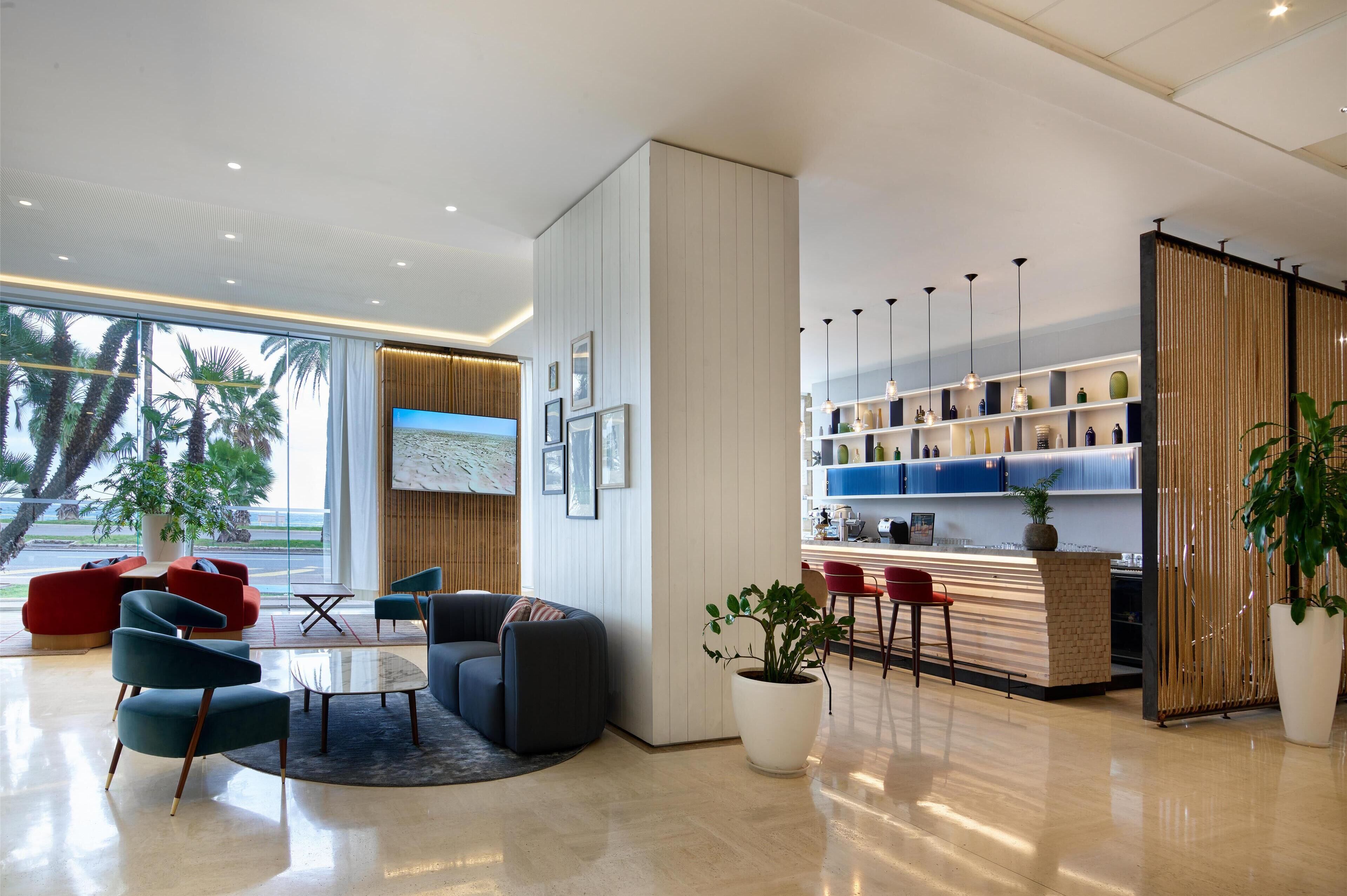 A modern lobby with a seating area, a reception desk, and a large window with a view of palm trees.
