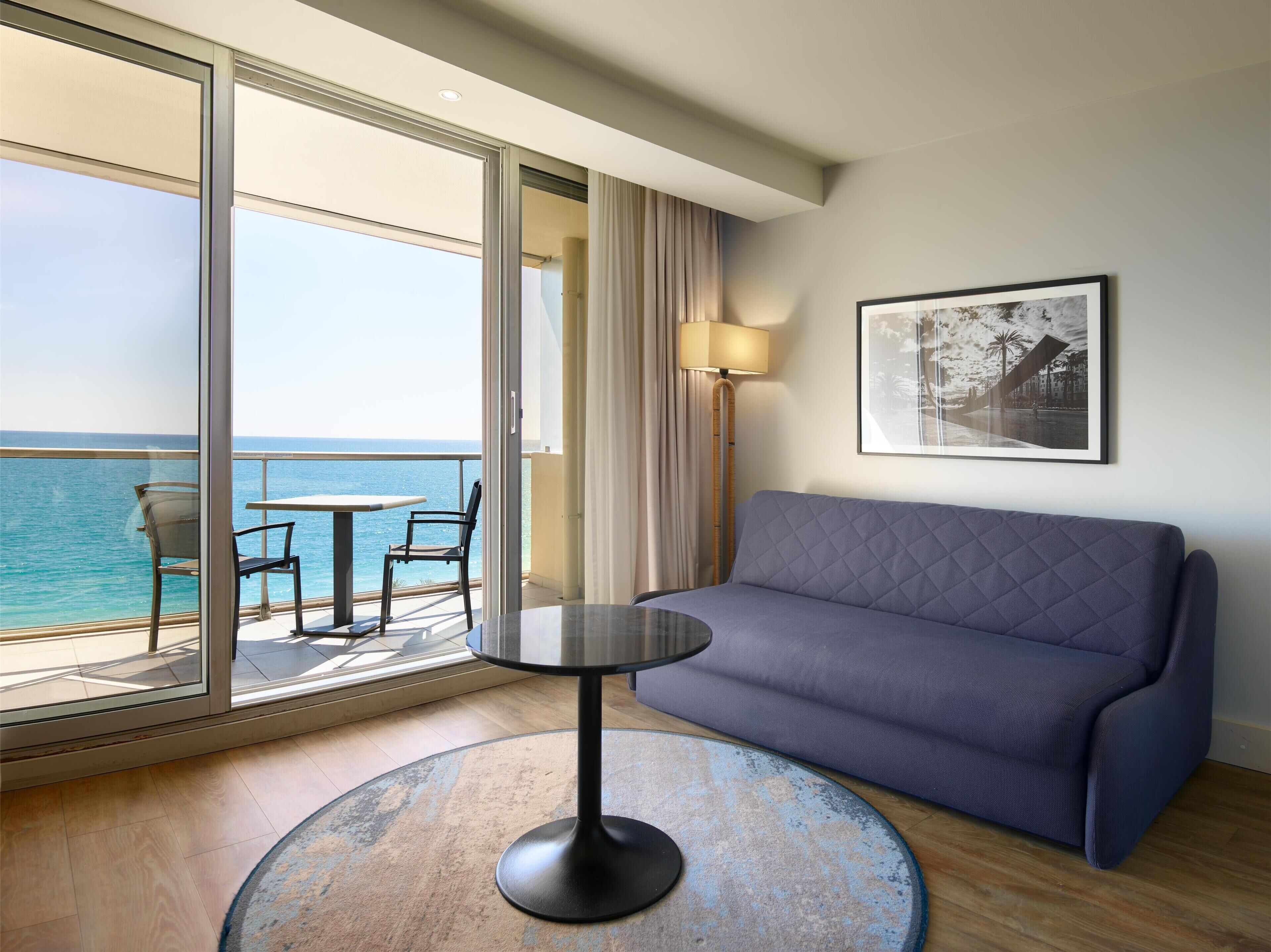 Une chambre d’hôtel avec un balcon, un canapé, une table et une lampe.
