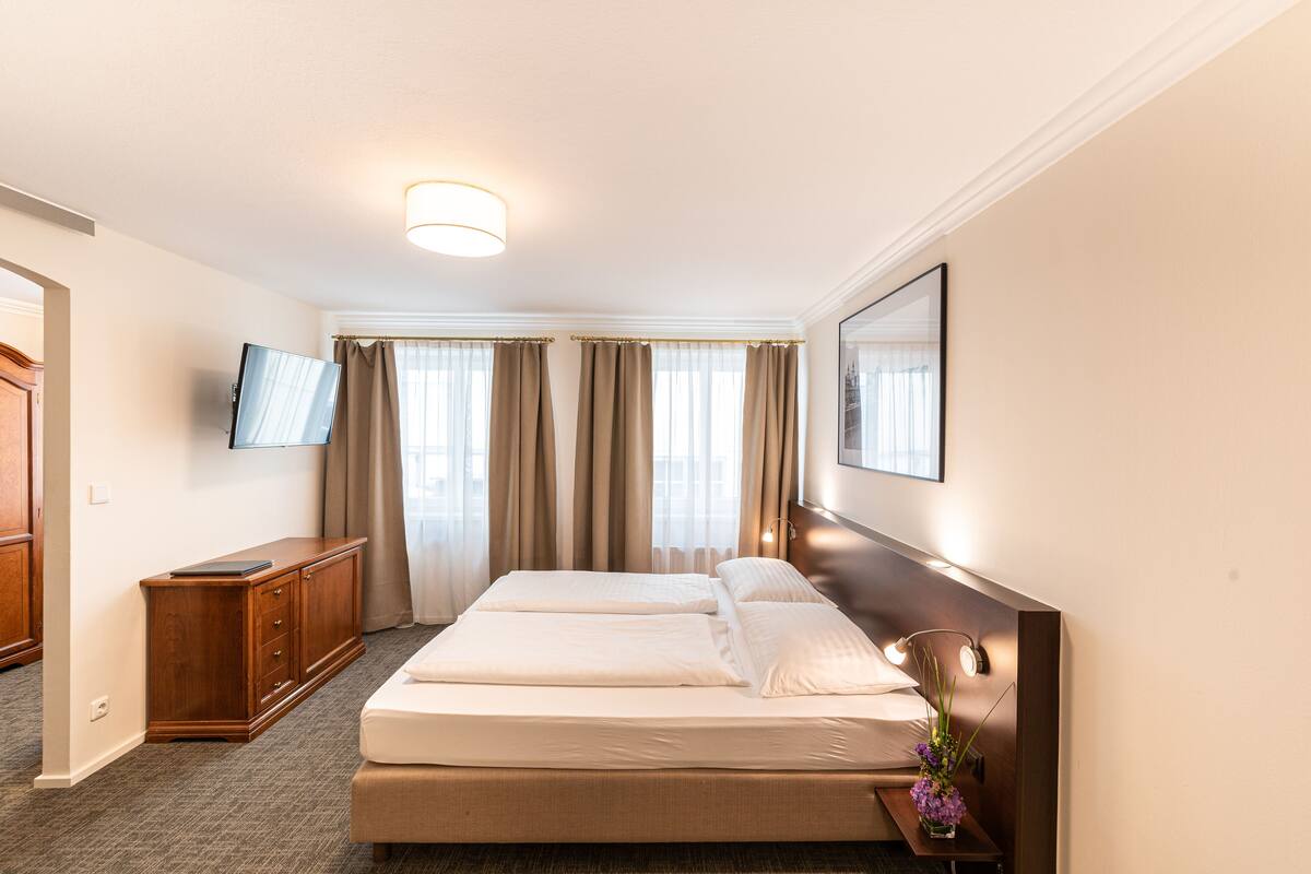 A hotel room with a large bed, a wooden dresser, a flat-screen TV, and a framed picture on the wall.
