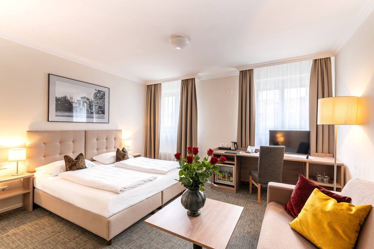 A hotel room with a large bed, a desk, a chair, a TV, and a vase with flowers.