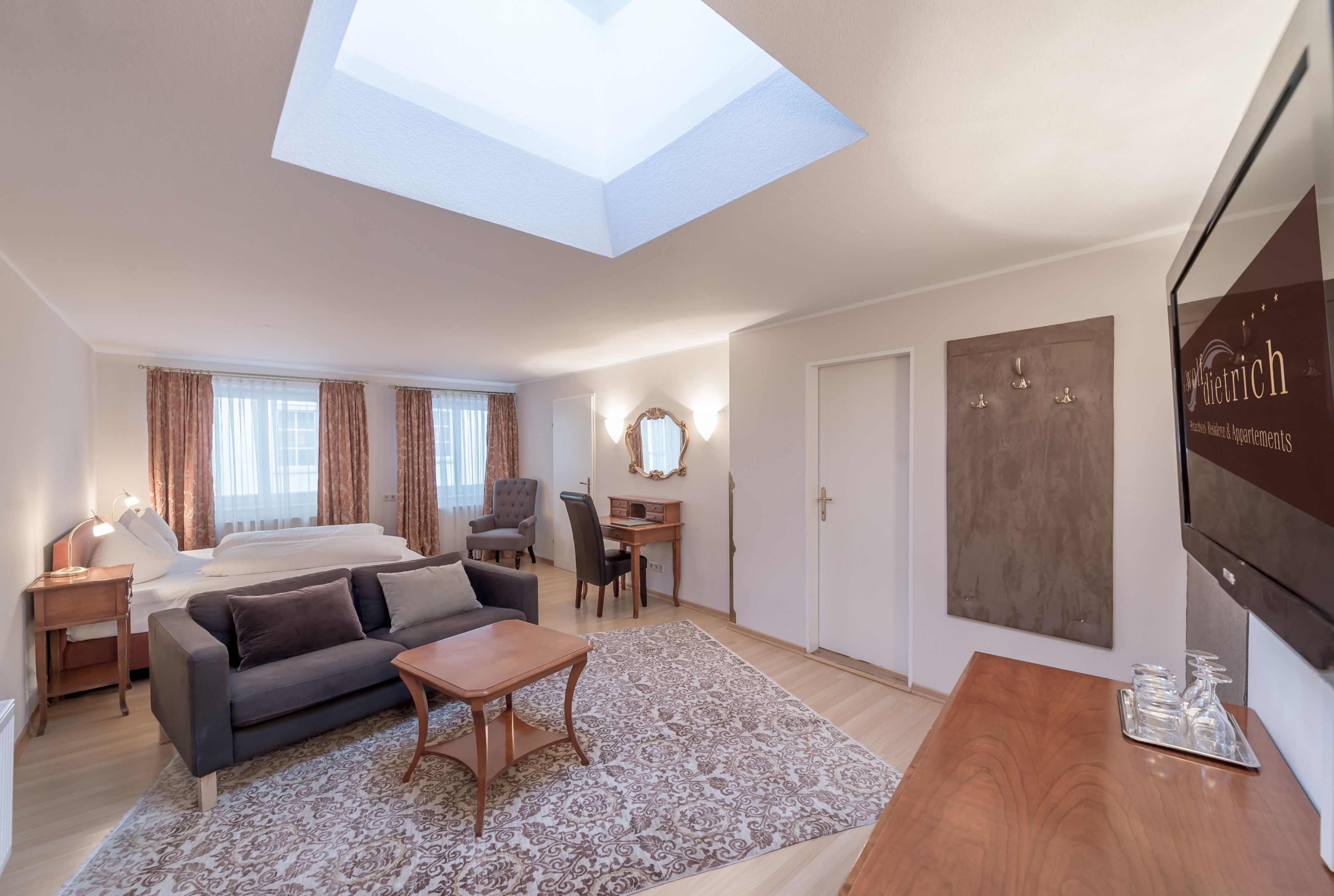 A modern hotel room with a skylight, a bed, a sofa, a desk, and a TV.