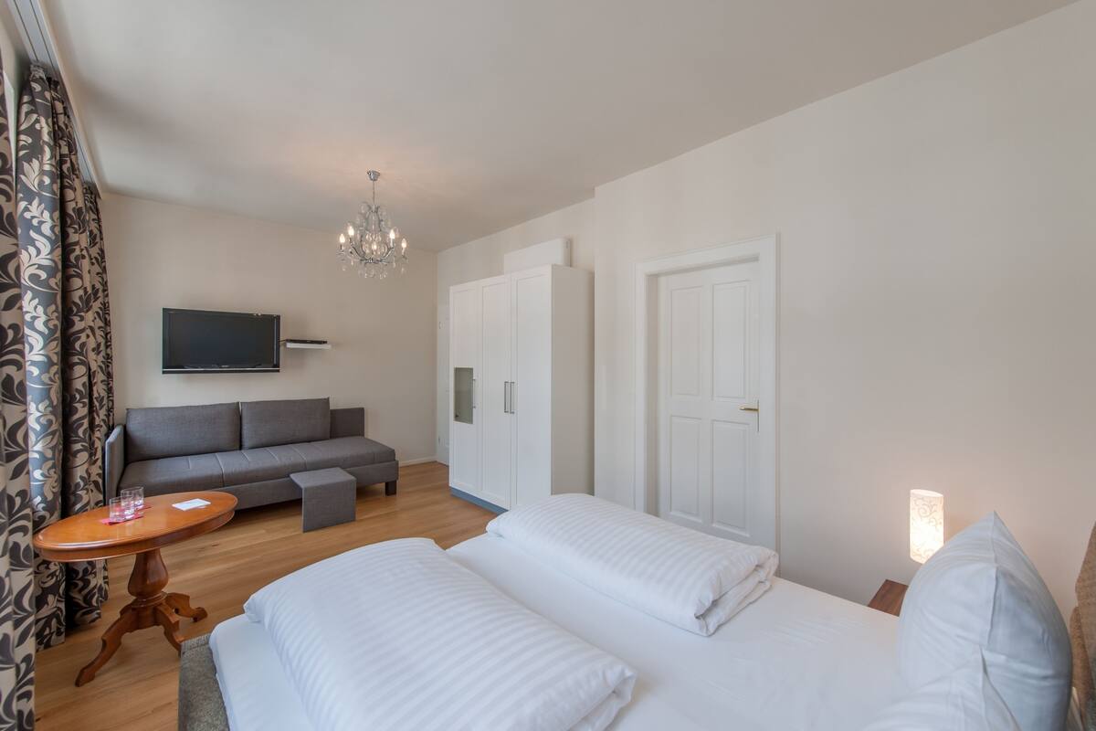 A hotel room with a bed, a sofa, a TV, a chandelier, and a wardrobe.