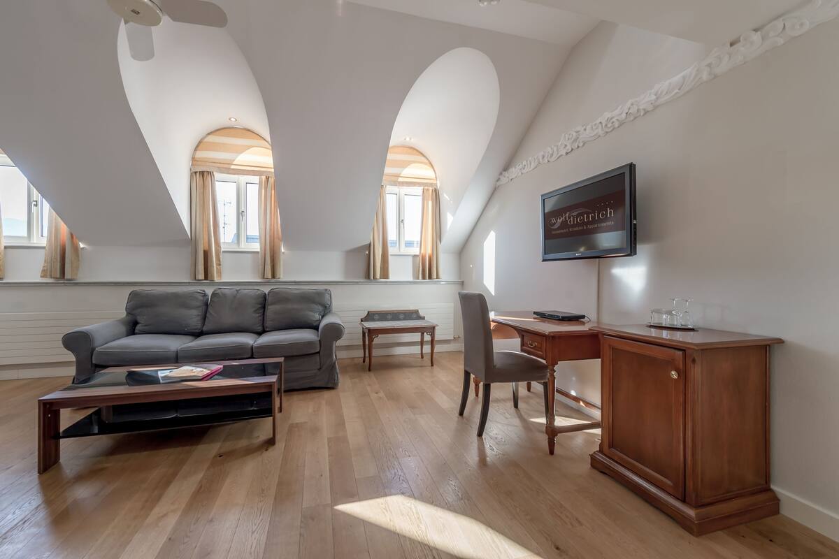 A spacious living room with a grey sofa, wooden coffee table, and a TV on a wooden cabinet.