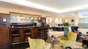 A bar area with a counter, bar stools, and hanging pendant lights. There are two armchairs and a small table with a vase. - Altstadthotel Wolf-Dietrich (Salzburg)