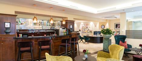 A bar area with a counter, bar stools, and hanging pendant lights. There are two armchairs and a small table with a vase.