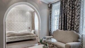 A bedroom with a tufted headboard bed, a sofa, a glass coffee table, and a view through an arched doorway. - Altstadthotel Wolf-Dietrich (Salzburg)