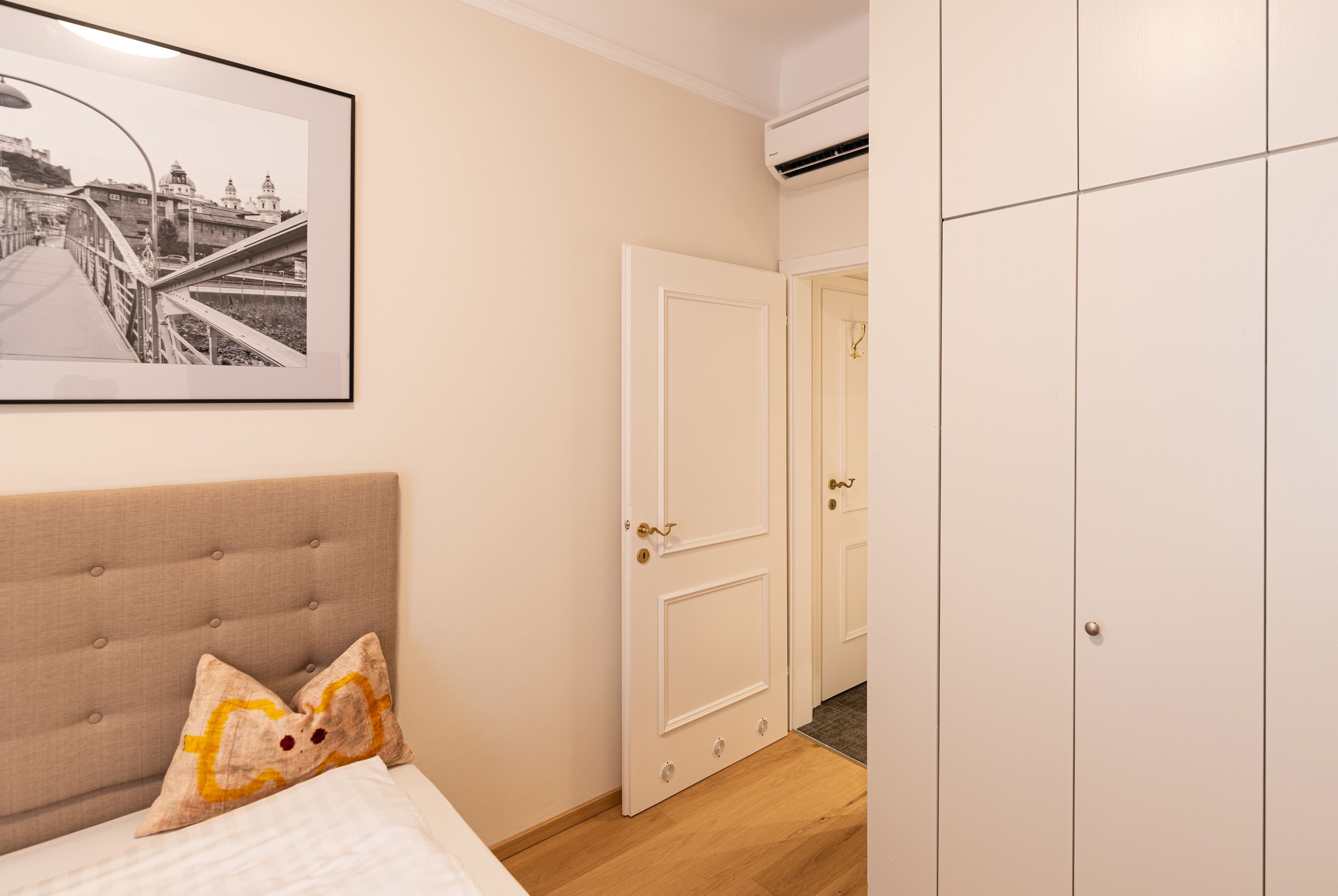 A bedroom with a bed, a headboard, a framed picture on the wall, and a wardrobe.