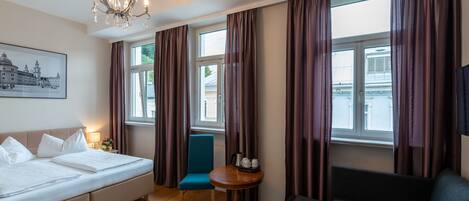 Habitación de hotel con cama, sofá, sillón, una pequeña mesa con hervidor y candelabro.