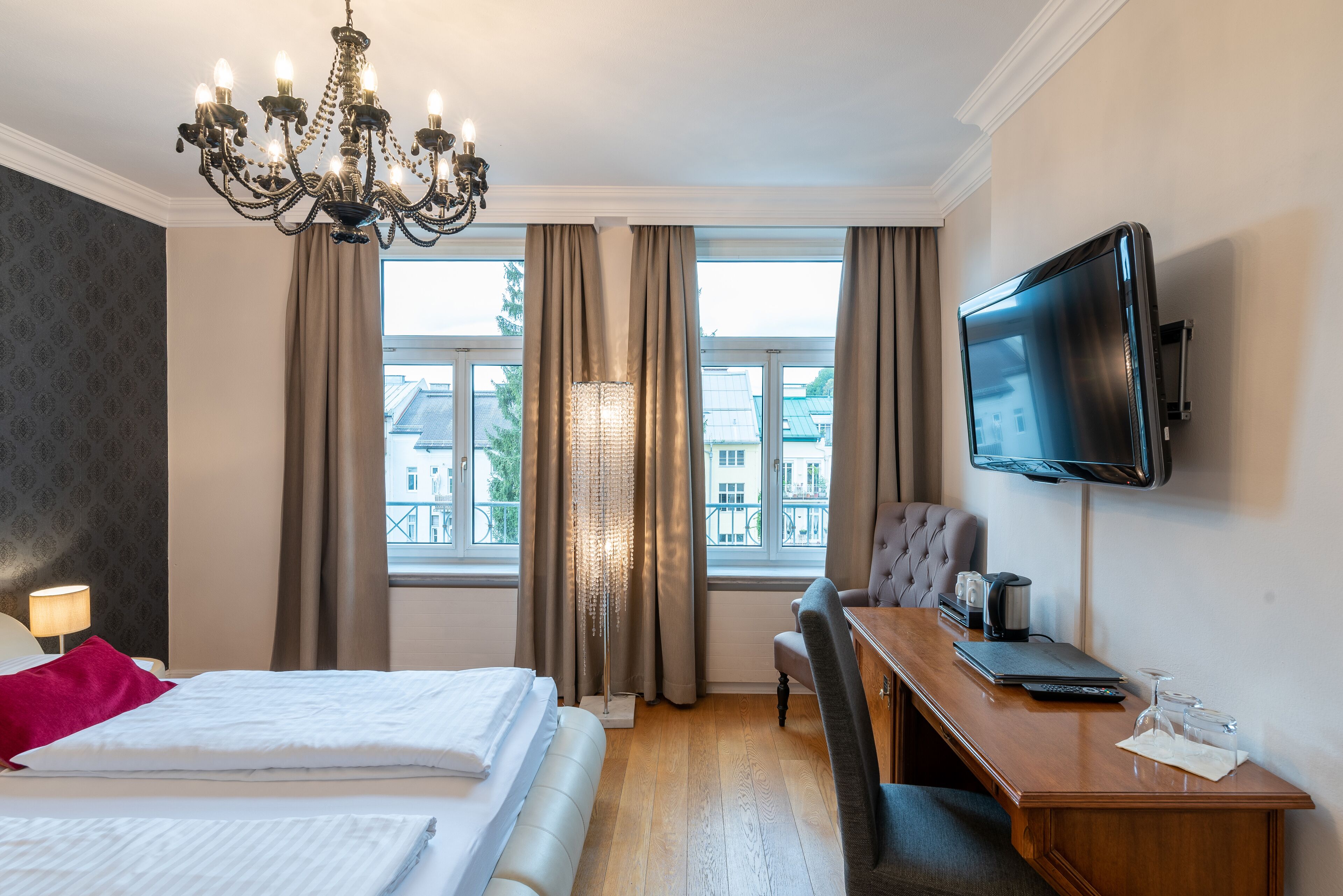 Habitación de hotel con cama, escritorio, televisión y vista a edificios a través de la ventana.