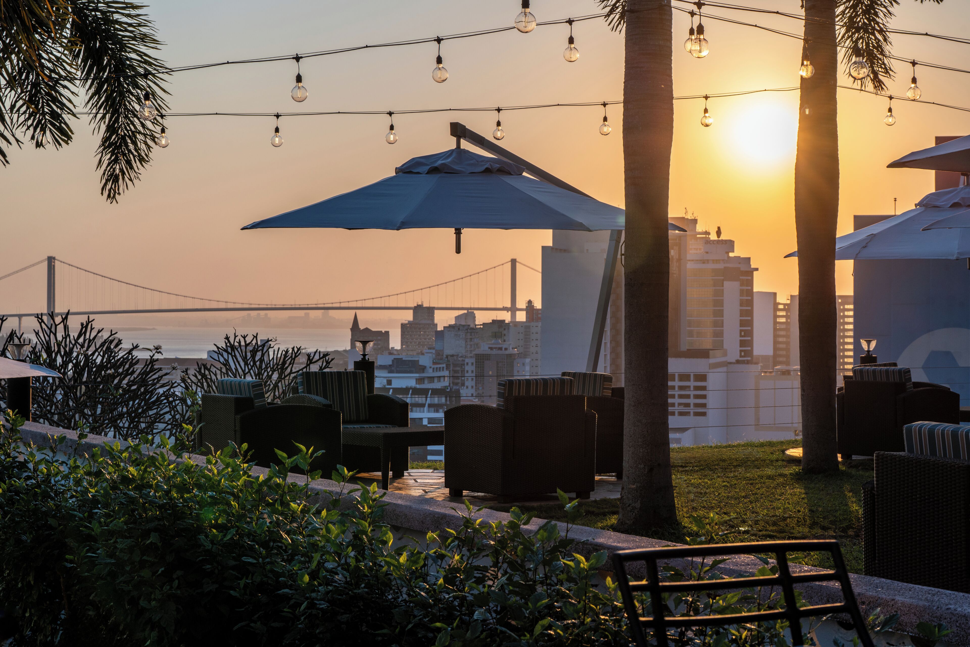 Outdoor seating with umbrellas, a view of a bridge, and city buildings in the background.