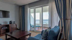 A hotel room with a wooden coffee table, a sofa, a TV, and a balcony with a view.