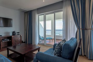 Habitación de hotel con una mesa de centro de madera, un sofá, un televisor y un balcón con vistas.