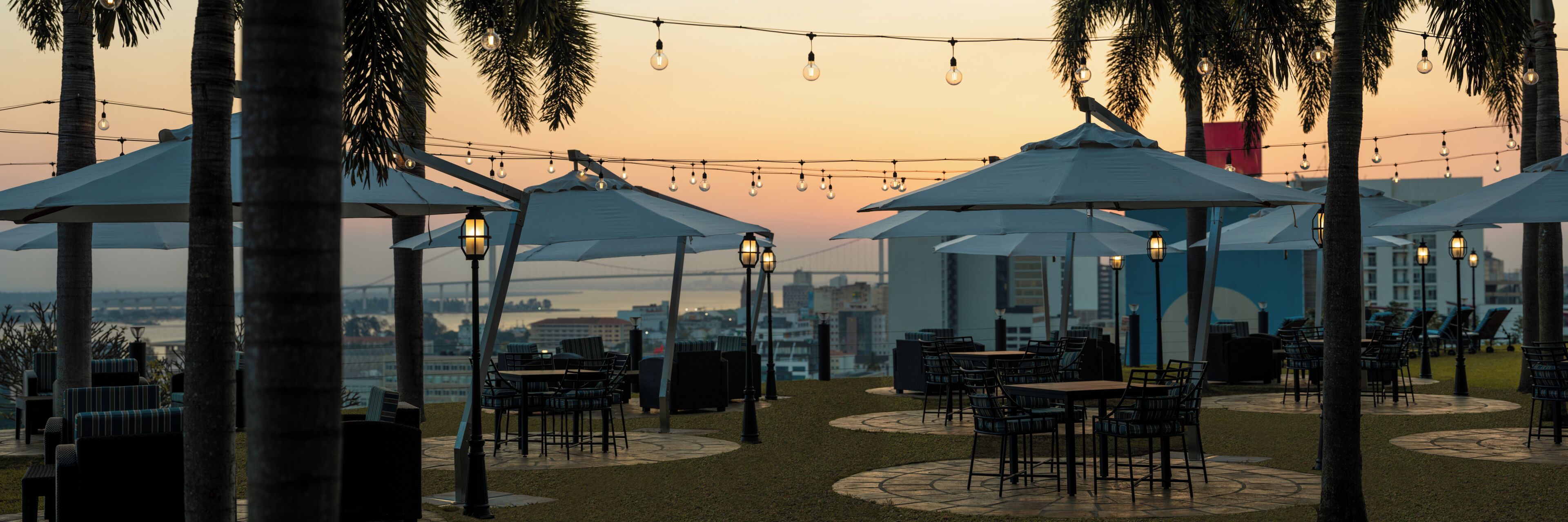 Espace extérieur aménagé avec des parasols, des tables et des chaises, offrant une vue sur le paysage urbain.