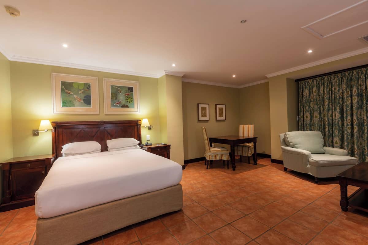 A hotel room with a large bed, a desk, two chairs, and two framed pictures on the wall.