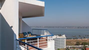 A balcony with a table, chairs, and a view of the sea and buildings.