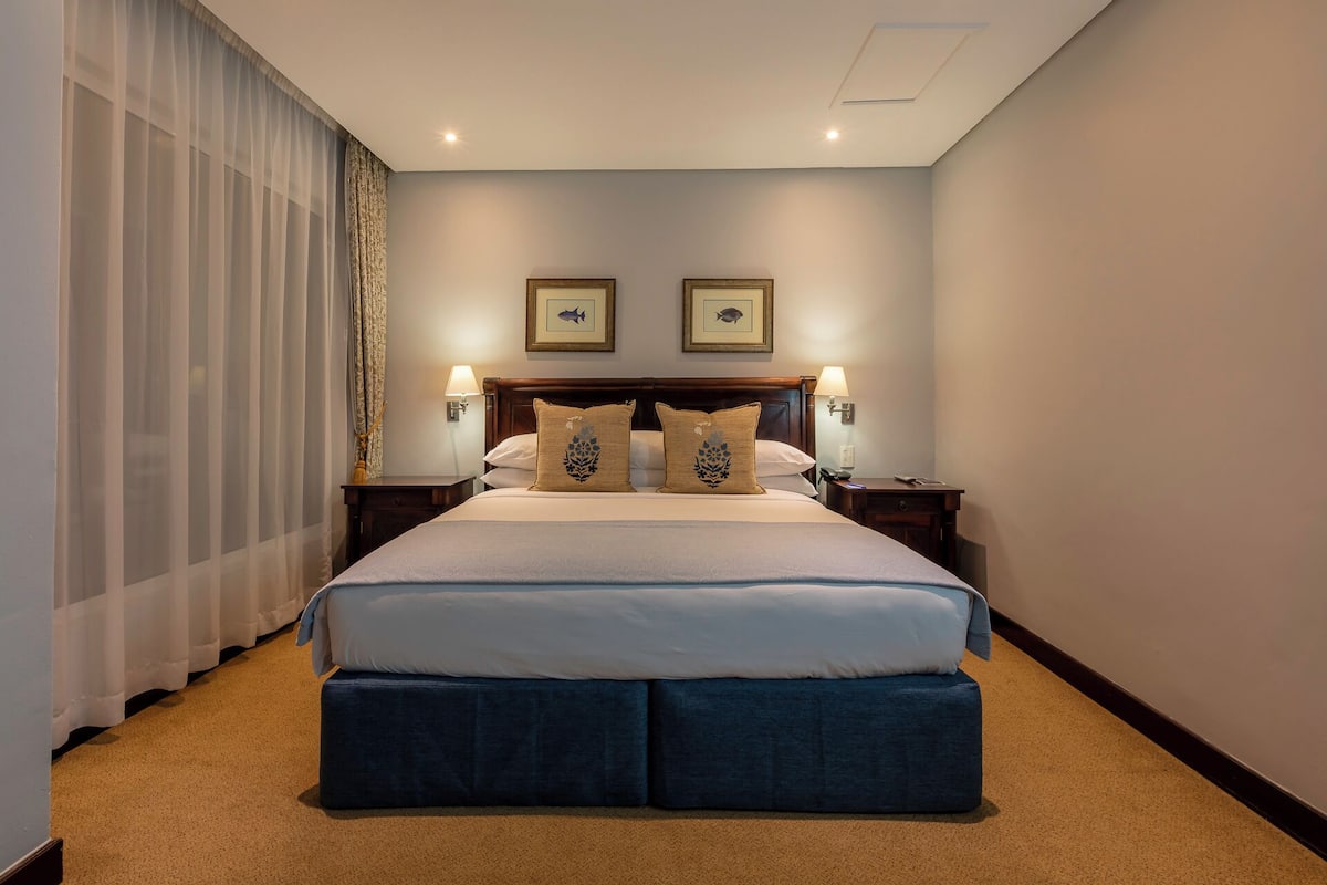 A hotel room with a large bed, two wall-mounted lamps, and a headboard with decorative pillows.