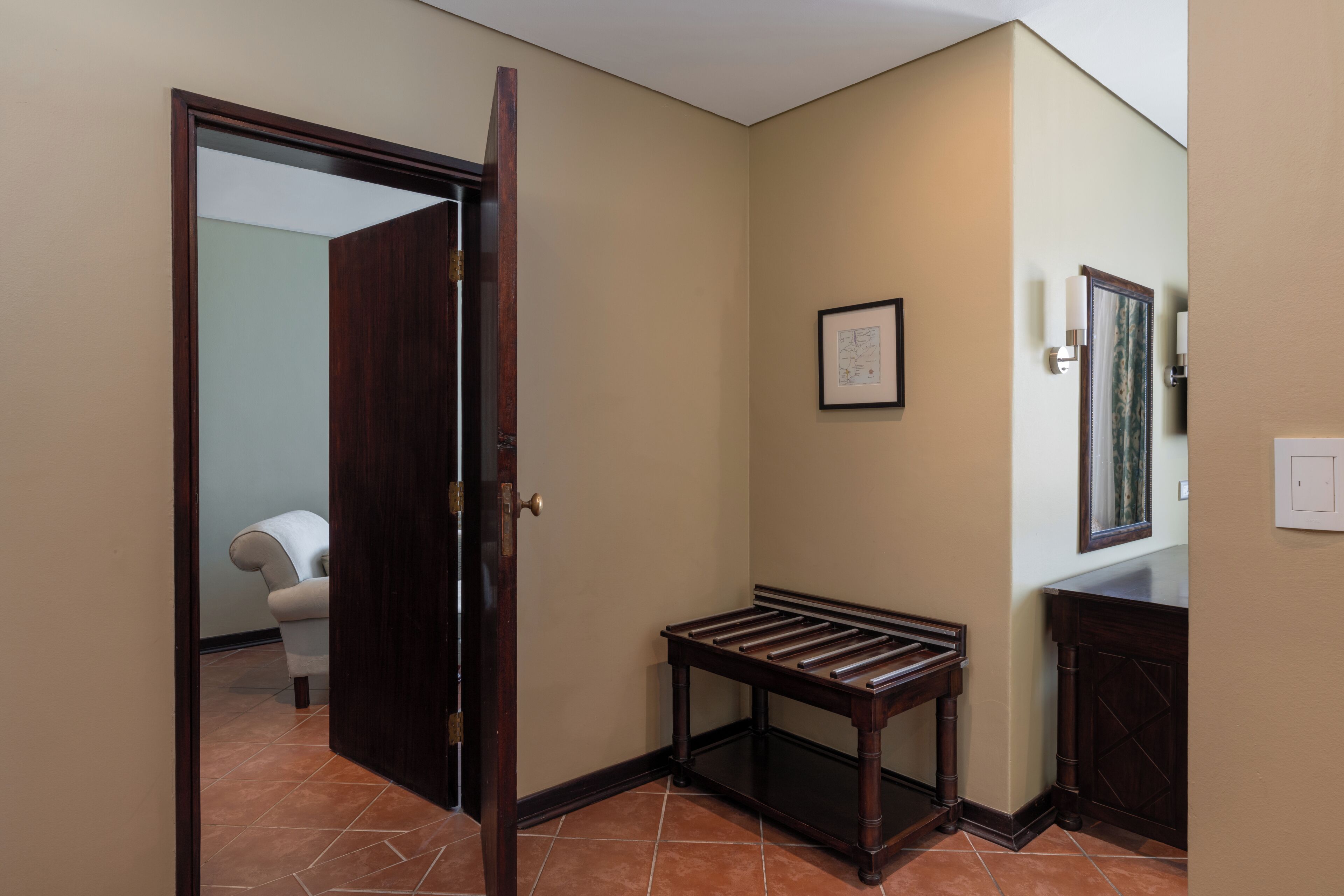 A hallway with a wooden bench, a door, a framed picture on the wall, and a tiled floor.