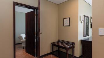 A hallway with a wooden bench, a door, a framed picture on the wall, and a tiled floor.