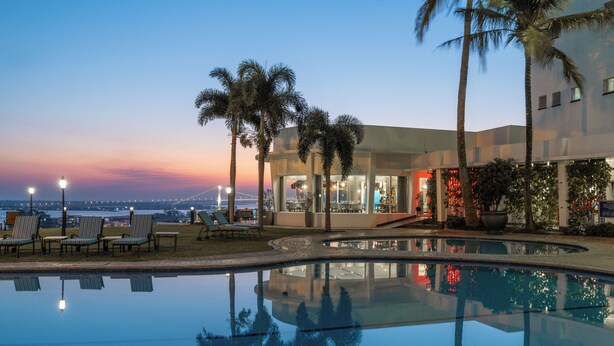 A pool area with lounge chairs, a building with large windows, and a sunset view. - Hotel Cardoso (Maputo)