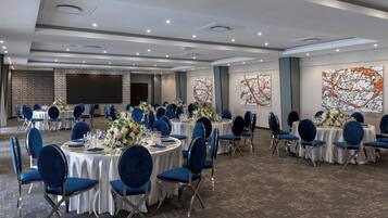 Un salón de banquetes con mesas redondas, sillas azules, manteles blancos y centros de mesa florales.