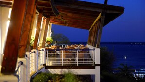 An outdoor dining area with wooden beams and a view of the sea at dusk. - Hotel Cardoso (Maputo)