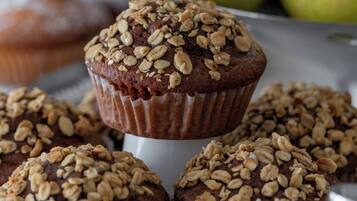 A tray of muffins topped with oats, with pears in the background.
