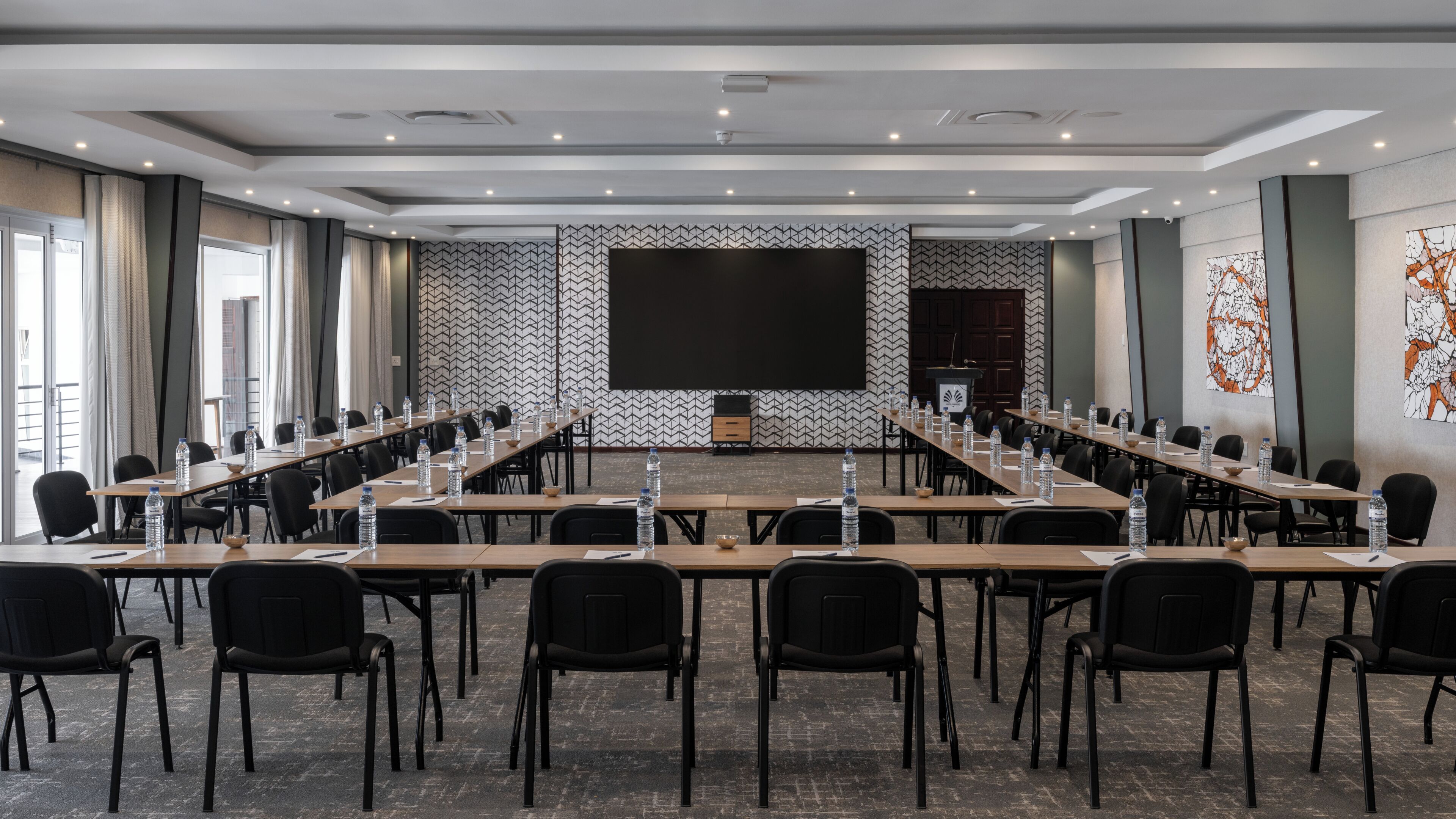 A conference room with a long table, chairs, a projector screen, and a podium.
