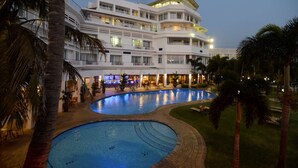 A multi-story hotel with a swimming pool, palm trees, and outdoor seating areas.