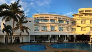 A multi-story hotel with a pool area, palm trees, and a clear sky.