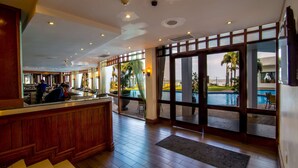 A hotel lobby with a reception desk, large windows, and a view of an outdoor swimming pool. - Hotel Cardoso (Maputo)