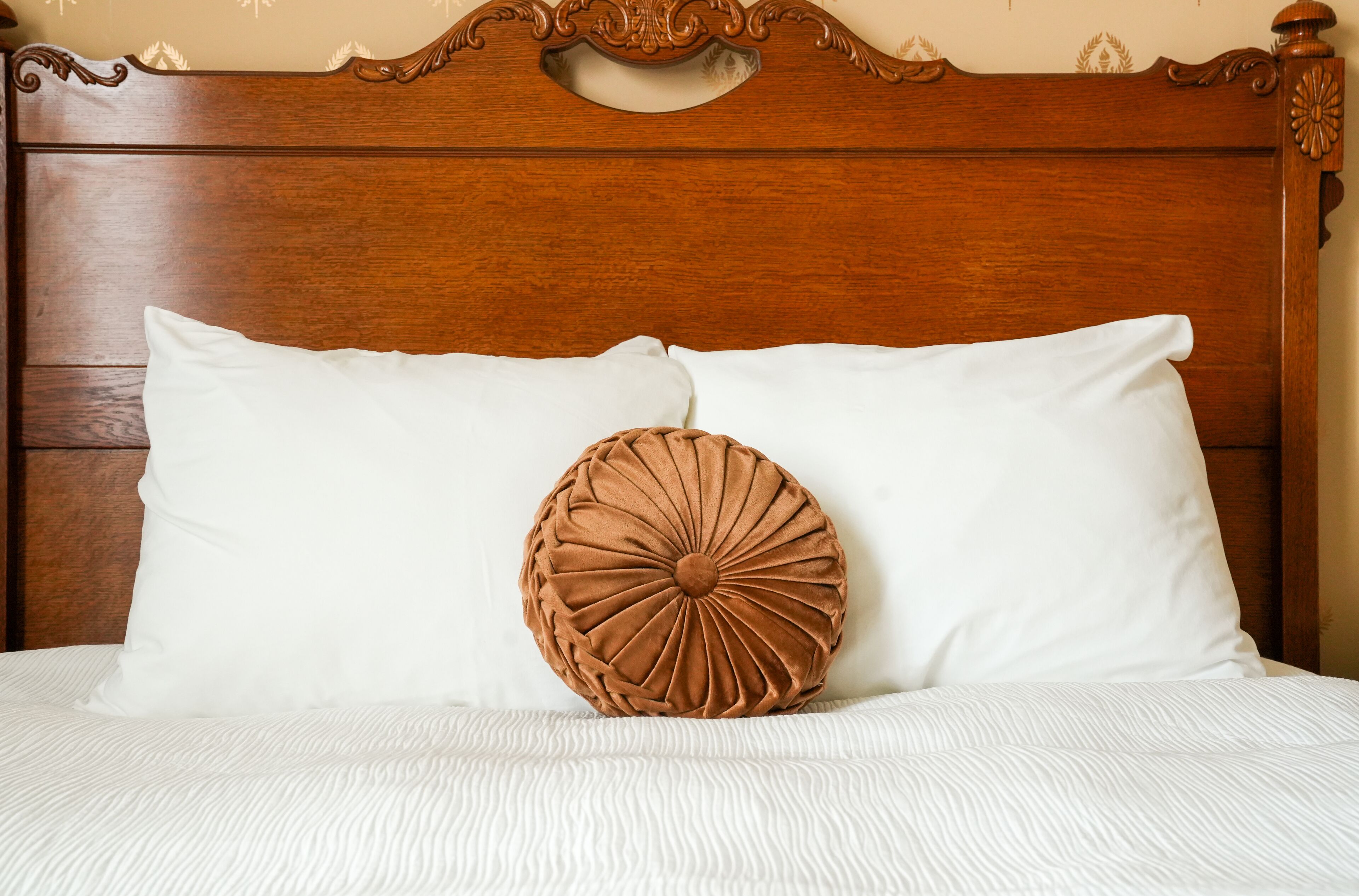 Ein Bett mit Holz-Kopfteil, zwei Kissen und einer weißen, strukturierten Tagesdecke.