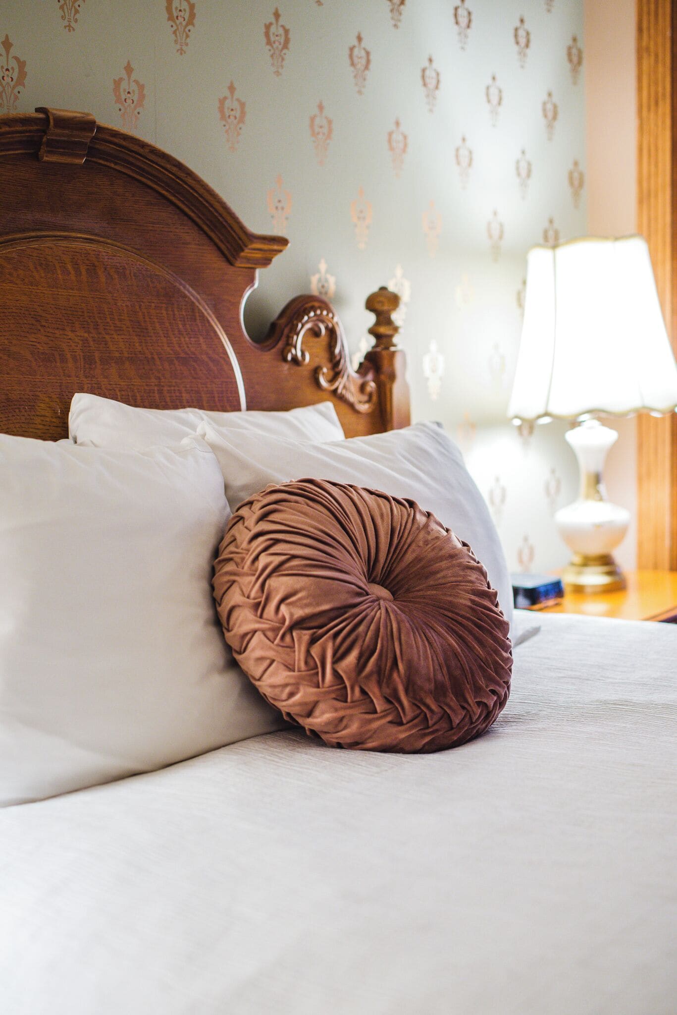 A neatly made bed with a wooden headboard, white and brown pillows, and a bedside table with a lamp.