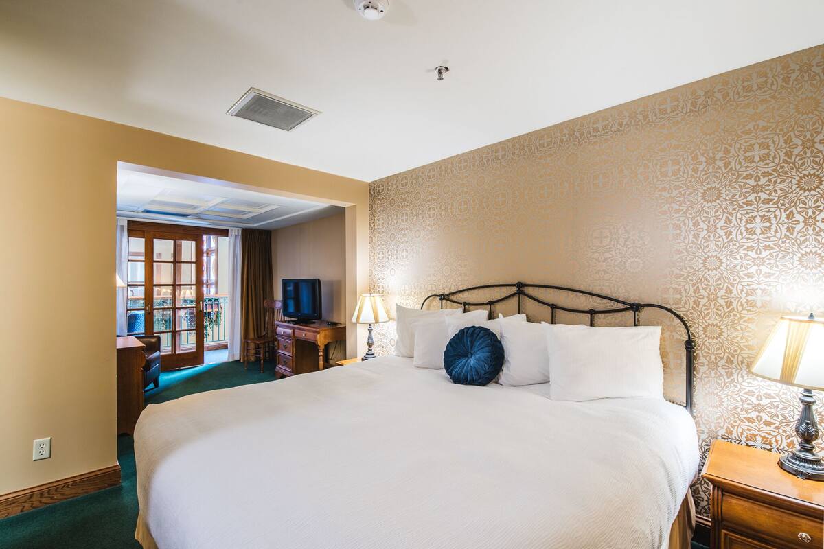 Habitación de hotel con una cama grande, un escritorio con computadora, una lámpara y un papel tapiz estampado.