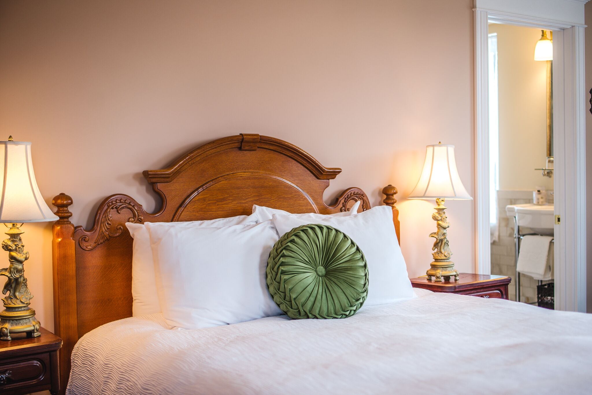 Una cama bien tendida con cabecera de madera, dos lámparas de noche y una almohada decorativa verde.