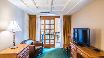 A hotel room with a wooden desk, a leather chair, a television, and a balcony door.