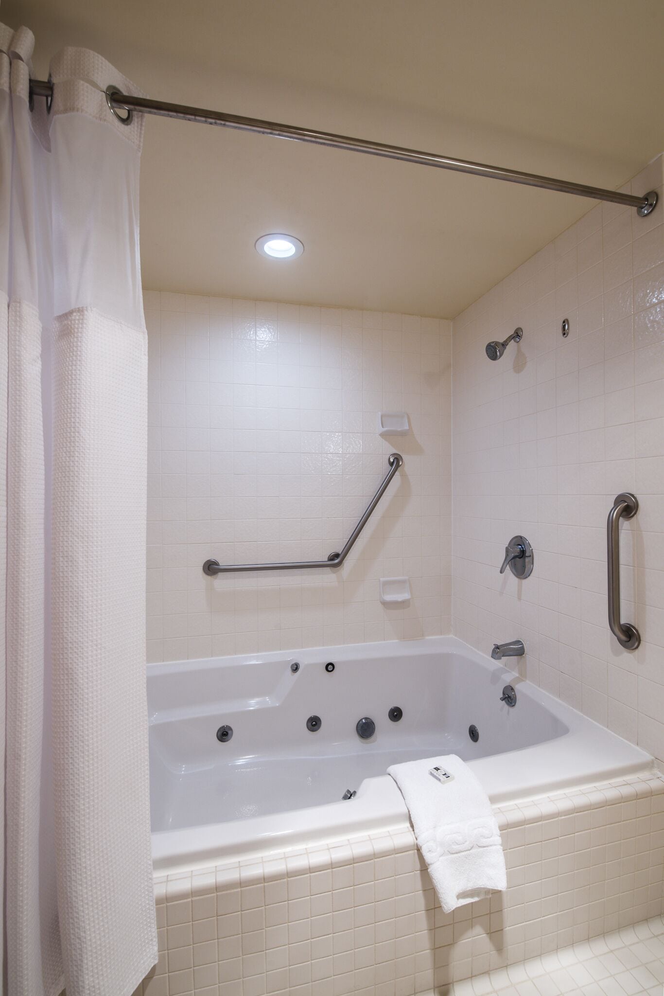A bathroom with a white bathtub, grab bars, a showerhead, and a towel on the tub.