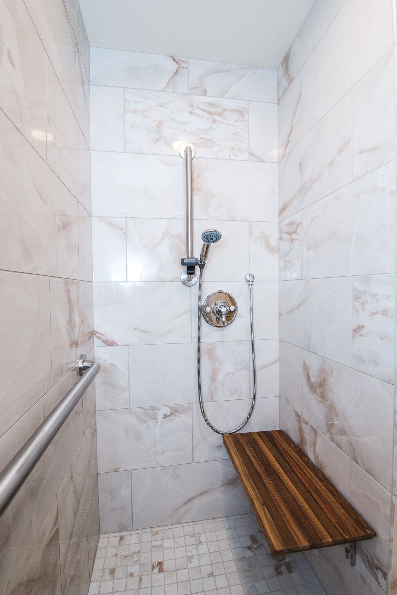 Ducha con cabezal de ducha manual y grifo empotrado en la pared, banco de madera y barandilla.