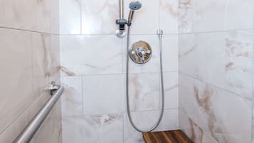 Ducha con cabezal de ducha manual y grifo empotrado en la pared, banco de madera y barandilla.
