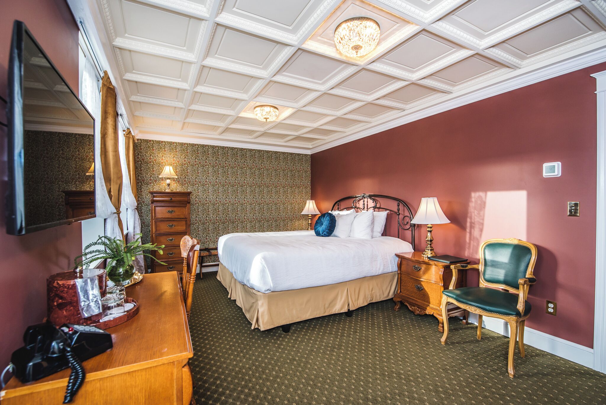 Een hotelkamer met een groot bed, een bureau met telefoon, een stoel, een nachtkastje met lamp en een spiegel aan de muur.
