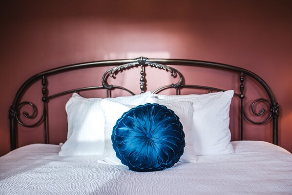 A bed with a metal headboard, white bedding, and a blue decorative pillow.
