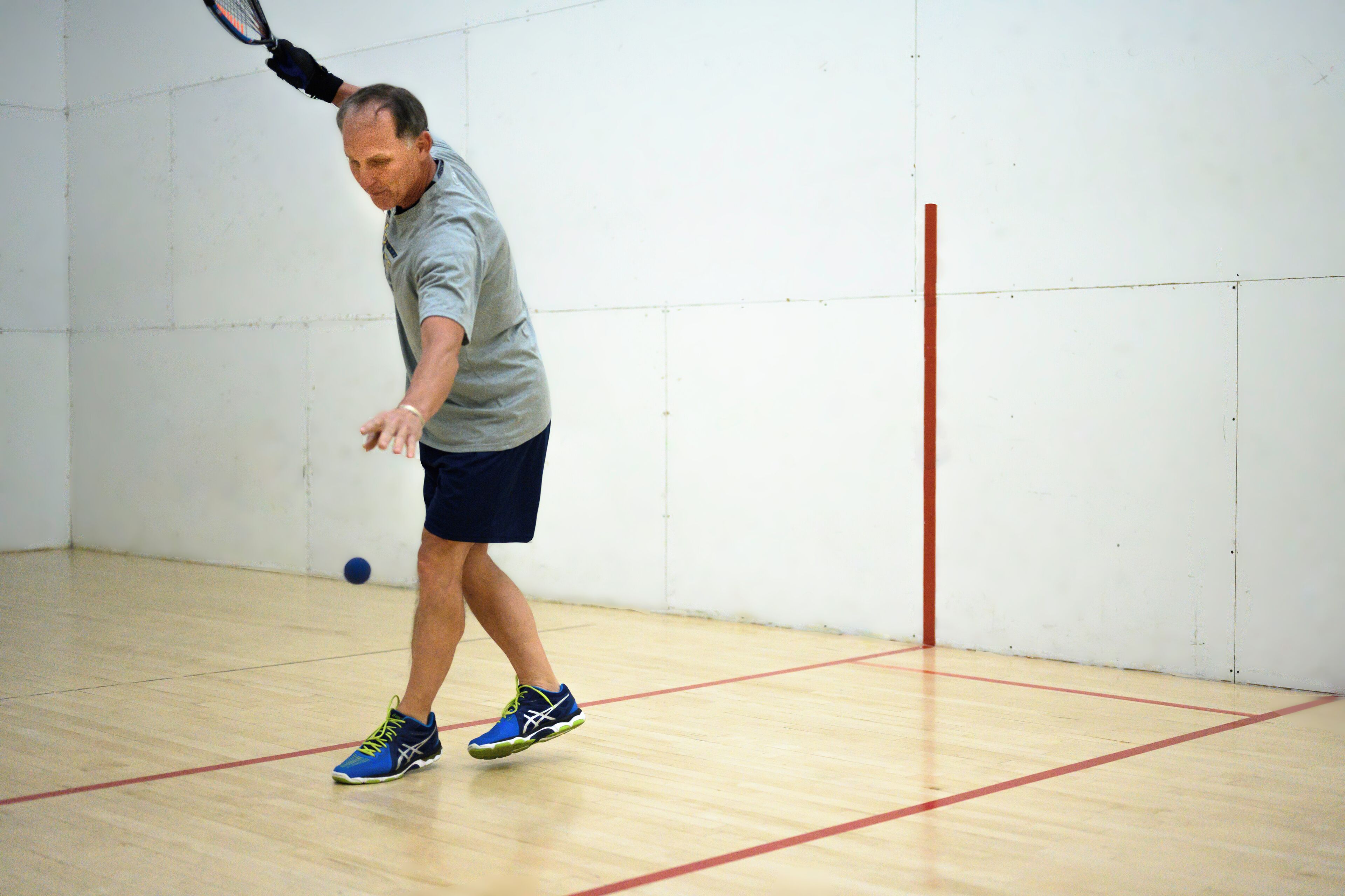 Un uomo che gioca a squash in una stanza con pavimento in legno e pareti bianche.