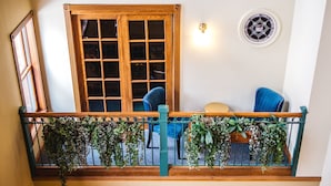 A balcony with wooden railings, a window with multiple panes, and two blue chairs.