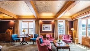 A room with a patterned carpet, wooden ceiling, and large windows with curtains.
